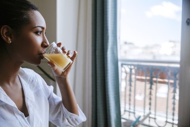 Young woman drinking glass of juice while looking through window