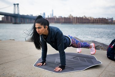 fit woman wearing a black hoodie and doing a plank outdoors with muscles shaking