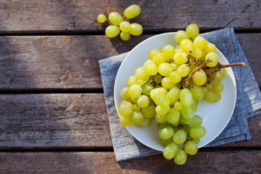 Grape on a white plate. Grey wooden background. Top view. Copy space.