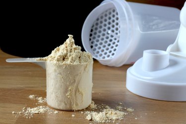 Protein powder in measuring cup next to shaker bottle lid