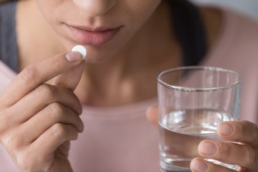 Close up of female about to swallow a pill with a glass of water.