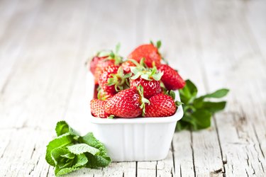 Fresh red strawberries in white bowl and mint leaves on rustic wooden background.