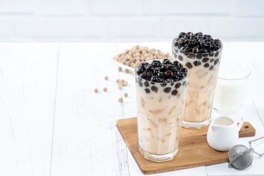 Bubble milk tea with tapioca pearl topping ingredient, famous Taiwanese drink on white wooden table background in drinking glass.