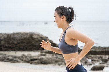 年轻的亚洲女人在沙滩上跑步。女孩在海边慢跑锻炼