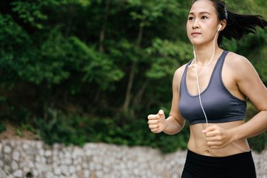 年轻的亚洲妇女运行在绿色的乡村。女孩在自然森林公园慢跑锻炼