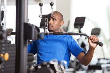 Man in a blue shirt using the lat pulldown machine at the gym