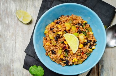 Black beans and rice with pepper cilantro zucchini  and a lime wedge in a blue bowl on gray wooden table next to a spoon