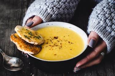 A woman on the soup diet eating carrot pumpkin cream soup with garlic bread