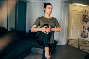 Image of fit young woman exercising at home, stretching legs in the room. Housewife warming-up muscles before workout doing stretching exercise sitting on floor at home.