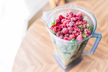 Macro closeup of fresh green kale and frozen raspberries in plastic blender container for smoothie