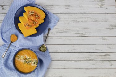 pumpkin cream soup in a blue plate on a white wooden background using light blue textile and spoons. flat lay. copy space