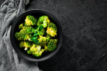 Boiled broccoli in a black plate. On a black background. Top view. Free space for your text.