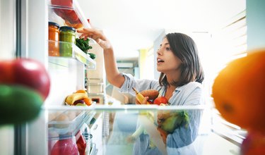 Woman picks out a handful of fruits and veggies from the fridge