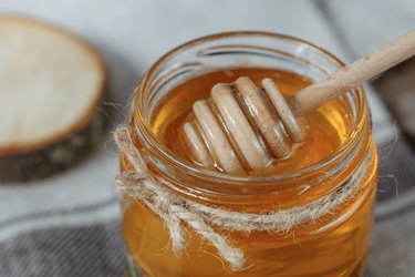 Glass pot of honey on a rustic bacground.