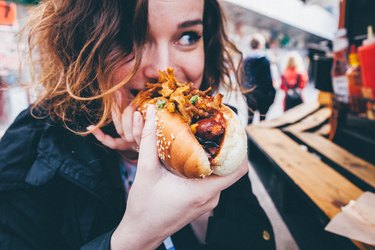 Close-Up Of Young Woman Eating Hot Dog On Street