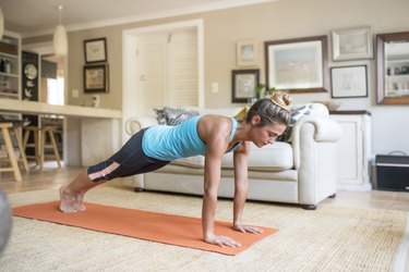 Woman practicing in plank pose on mat at home