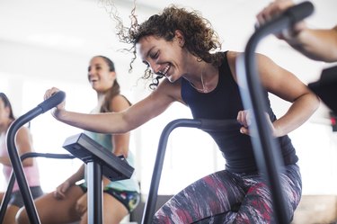 smiling, playful fit women using elliptical bike in gym