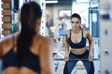 Woman lifting barbell in gym looking in mirror