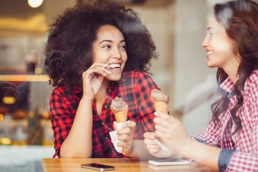 two young adults holding ice cream cones smiling at each other at a wooden cafe table