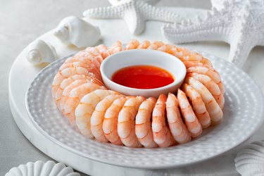 Close-up on shrimp ring with sweet chili sause on light table with white sea decorations