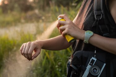 A woman using mosquito repellent while hiking in the woods