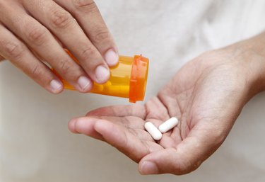 a close up photo of a person pouring two white pills into their hand from an orange prescription bottle