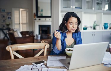 A woman eating a healthy lunch and reviewing her weight-loss program on her laptop