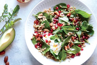 Pomegranate-Farro Breakfast Salad With Honey Ricotta on a white plate over gray background.