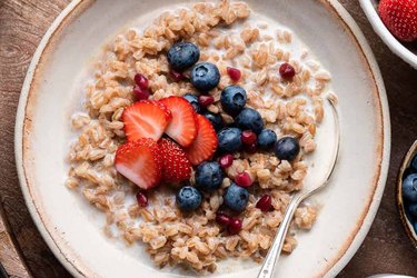 Maple Cinnamon Breakfast Farro with berries in a white bowl with spoon on wooden table