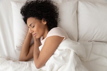 overhead photo of woman sleeping on white pillows and sheets