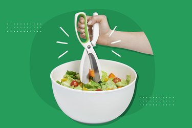 hand using salad scissors in white salad bowl on green background