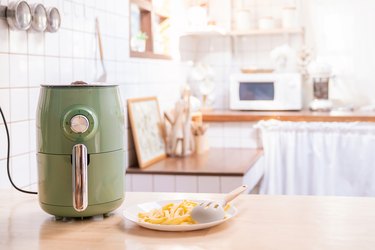green air fryer on kitchen counter with plate of fries beside it