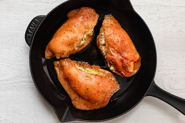 Three stuffed and cooked chicken breasts on a cast iron skillet