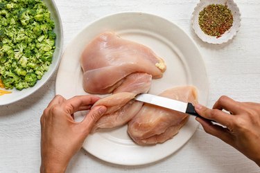 A photo of raw chicken breast on a plate, being cut horizontally at the thickest part
