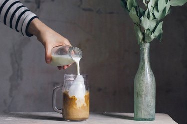 woman hand pouring milk into coffee mason jar with plant next to it