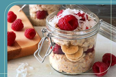 Glass jar of overnight oats with raspberries and shaved coconut on a counter