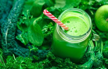 Anti-inflammatory Drink Super Green Smoothie in a mason jar with straw on a bed of leafy greens