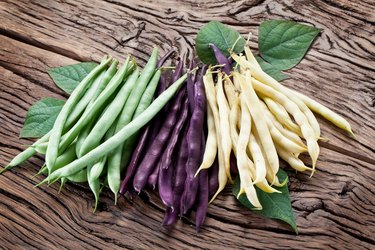 Purple, green and yellow beans lying on a wooden table