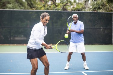 senior couple playing doubles tennis together outside