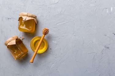 Top view of glass jars with honey with wooden drizzler on grey background to illustrate if a 3-year-old can have honey