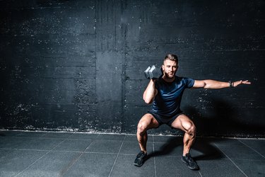 Young strong fit muscular sweaty man with big muscles strength cross workout training with dumbbells weights in the gym dark image with shadows real people