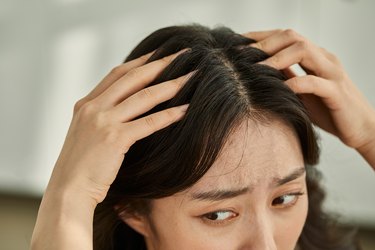 Asian person assigned female at birth running fingers through her hair with a concerned expression wondering why does my hair hurt