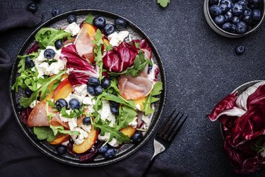 Delicious salad  with arugula, radicchio, peaches, prosciutto, feta cheese and blueberries. Black table background, top view