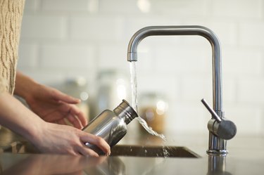 Filling a reusable water bottle with tap water in the kitchen sink.