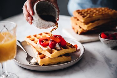 pouring maple syrup on plate of Belgian waffles on kitchen table