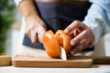 close view of a person slicing a fresh tomato on a wooden cutting board