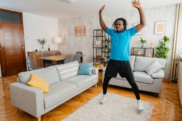 Adult in blue tee and black bottoms doing jumping jacks in living room