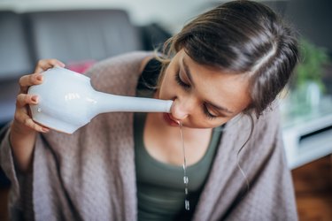 A person with long brown hair doing nasal irrigation as a natural remedy for sore throat