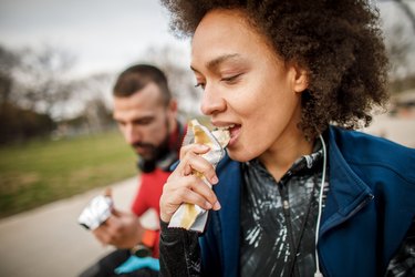 woman eating a granola bar to represent oats' benefits and side effects from eating too much oatmeal and digestive first cereal