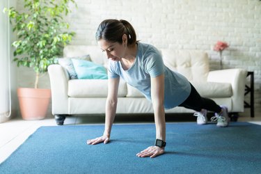 woman wearing a smartwatch and doing a push-up workout on a blue mat in her living room